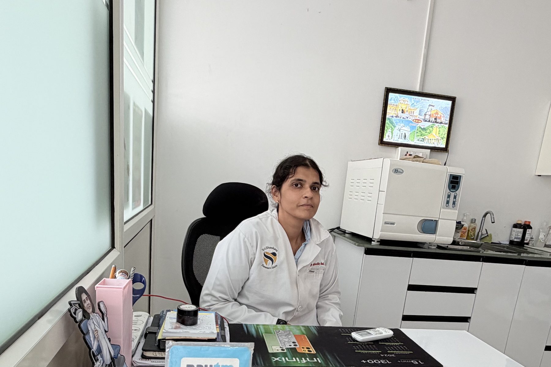 Dr. Advaitha Anand at her desk in the clinic, with the autoclave and instrument preparation area behind her.
